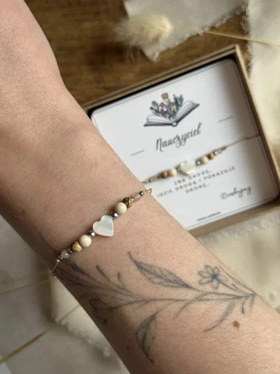 Zbliżenie na serce z masy perłowej i jaspis krajobrazowy w bransoletce na beżowym sznurku.