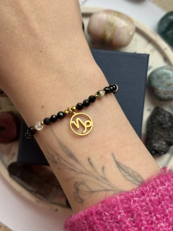 Zodiakalna bransoletka Cosmic Aura ze złotym znakiem Koziorożca prezentowana na kobiecym nadgarstku.