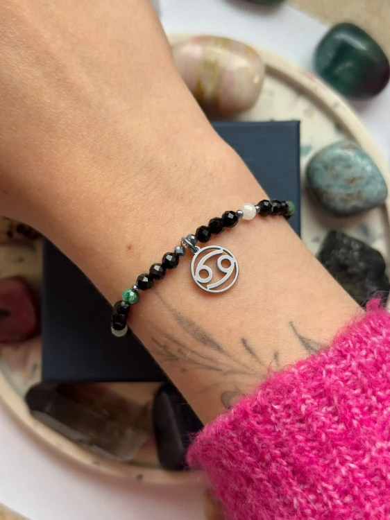 Ochronna bransoletka dla Raka ze srebrną zawieszką zodiakalną na nadgarstku modelki.