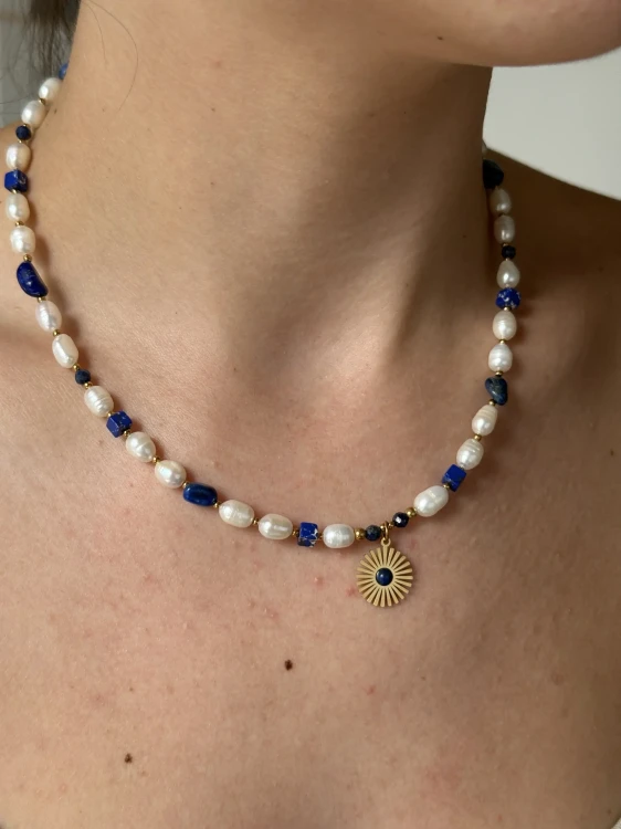 Kobieta nosząca elegancki naszyjnik z naturalnych pereł i ciemnoniebieskich kamieni ze słoneczną zawieszką.