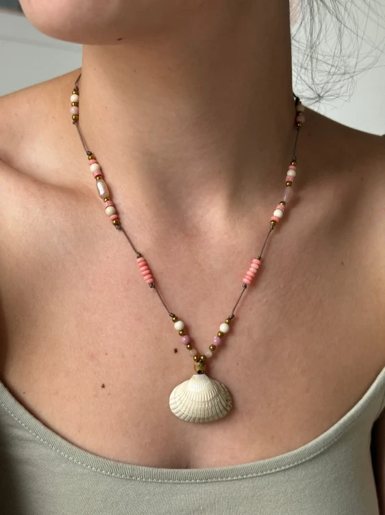 Kobieta nosząca naszyjnik z muszelką wyregulowany jako krótki choker blisko szyi.